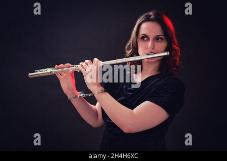 Musicista donna con un flauto in mani con polsini su uno sfondo scuro dello studio. Problemi di riproduzione musicale ai concerti, il concetto di non-libertà e a Foto Stock