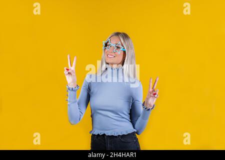 Ritratto di una ragazza allegra e alla moda che indossa occhiali da sole a forma di stella e mostra pace o segno di vittoria. Primo piano di bella donna Foto Stock