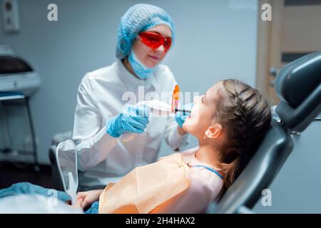 Dentista femmina che fornisce restauro dentario e riempimento con polimerizzazione UV lampada per bambino Foto Stock