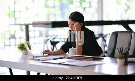 Una donna d'affari soffre di un mal di testa mentre lavora sui dati finanziari. Lavoratore femminile pensivo e stressato. Foto Stock