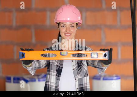 attraente lavoratrice di costruzione femminile in colore rosa hardhat tenuta livella spirito Foto Stock