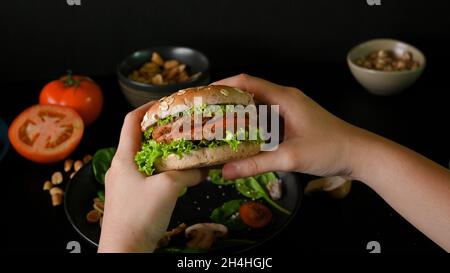 Le mani femminili tengono un delizioso hamburger a base di piante vegane con verdure fresche e gustosa salsa. Foto Stock