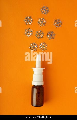 Bottiglia vuota di spray nasale e fiocchi di neve decorativi su sfondo arancione Foto Stock