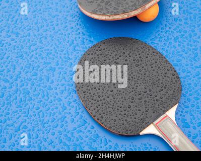 Paddle e palline da ping-pong, che sono state lasciate durante la pioggia. Ping-pong. Attrezzature sportive sul tavolo da ping pong Foto Stock