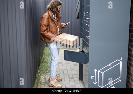 Donna che mette il pacco alla cella del terminale del posto Foto Stock