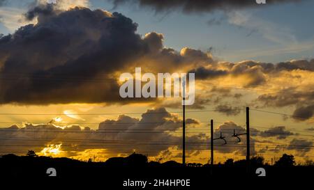 Il cielo del tramonto con le nuvole e le linee aeree del treno come sfondo Foto Stock