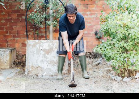 forte giovane uomo di mezza età danzante preparato con abbigliamento da giardinaggio nel giardino della sua casa. concetto di giardinaggio Foto Stock