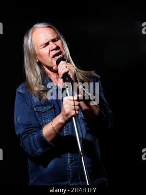 l'uomo anziano con lunghi capelli grigi in denim blu canta in un microfono sul palco su sfondo nero Foto Stock