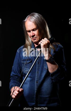 l'uomo anziano con lunghi capelli grigi in denim blu canta in un microfono sul palco su sfondo nero Foto Stock