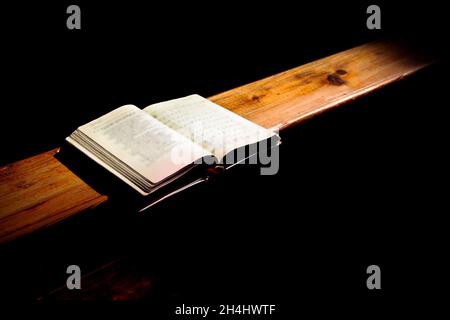 L'hymnbook si trova aperto su una panca della chiesa ed è illuminato con una luce morbida Foto Stock