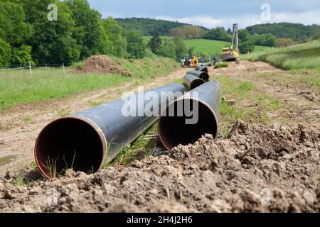 Gasdotto che si posa in campagna con due tubi del gas in primo piano e macchine per la posa di tubi con altri tubi nel backgr Foto Stock