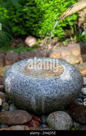 Zen fontana dalla parte anteriore in pietra di granito che si erge su grandi mattoni con insenatura di bambù acqua Foto Stock