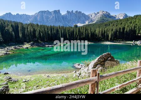 Lago di montagna turchese con una ringhiera nel mezzo della foresta e alte montagne sullo sfondo Foto Stock