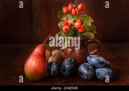 pere e prugne con un ramo di rosa selvaggia su sfondo di legno scuro in stile rustico Foto Stock