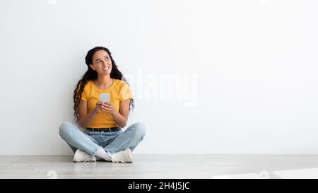 Offerta mobile. Sorridendo giovane donna che tiene smartphone e guardando da parte con interesse Foto Stock