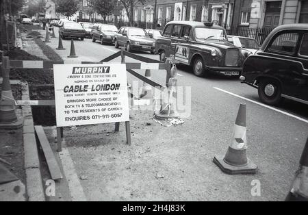 Una trincea scavata nella strada per stendere i cavi per Cable London Limited a Camden, Londra il 2 ottobre 1991. Foto Stock