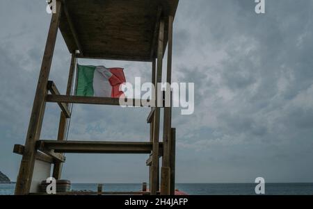 Torre di bagnino sulla spiaggia con bandiera italiana attraverso il cielo blu. Concetto di sicurezza sulla spiaggia Foto Stock