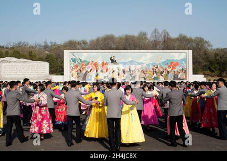 Gli studenti di Pyongyang ballano di fronte a un murale di Kim il-Sung per celebrare il giorno del Sole in Corea del Nord, aprile 2019 Foto Stock