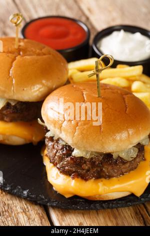 Hamburger classici al burro con patatine fritte e salse da vicino su un asse di ardesia sul tavolo. Verticale Foto Stock