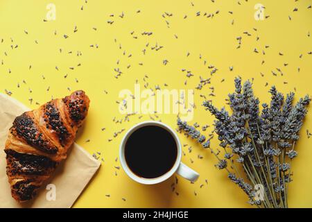 mattina di lavoro con tazza di caffè caldo, croissant dolce e bouquet di lavanda su sfondo giallo. Vista dall'alto, spazio di copia, mockup. Disposizione piatta. Foto Stock