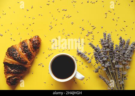 mattina di lavoro con tazza di caffè caldo, croissant dolce e bouquet di lavanda su sfondo giallo. Vista dall'alto, spazio di copia, mockup. Disposizione piatta. Foto Stock