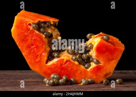 fetta fresca di papaya dolce o papaw, fettina di frutta dai colori vivaci con semi su un tavolo di legno, primo piano Foto Stock