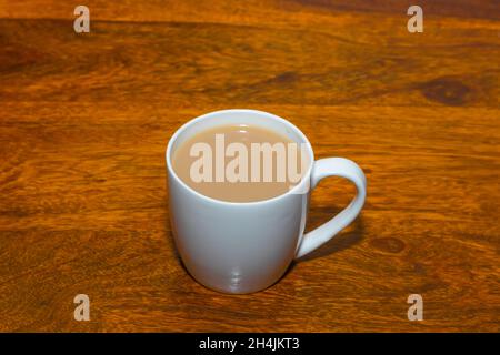 Tè fatto con latte servito in una tazza di ceramica bianca su un tavolo di legno Foto Stock