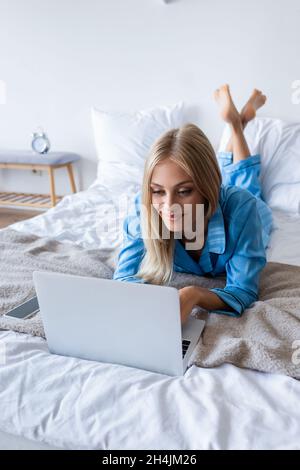 felice giovane donna in pigiama utilizzando il portatile in camera da letto Foto Stock