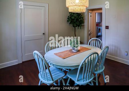 Una piccola sala da pranzo con un'illuminazione in rattan di tendenza e un tavolo da pranzo dipinto di blu Foto Stock