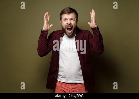 L'uomo caucasico bearded è infastidito, grida furiosamente e fa un gesto con le sue mani. Sfondo verde. Foto Stock