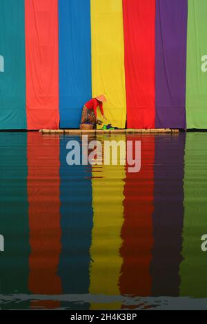 Donna in piedi su una zattera di fronte a uno sfondo multicolore che raccoglie i vestiti, Indonesia Foto Stock