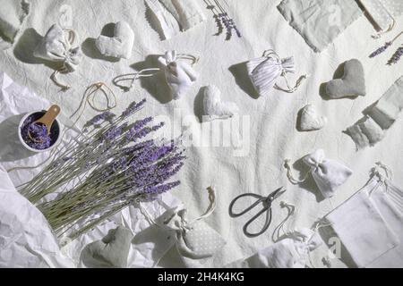 Bustine di lavanda fatte a mano in sacchetti di tessuto e cuori morbidi. Fiori secchi di lavanda per ripieno, forbici e candela. Giacitura piatta su tessuto di lino Foto Stock