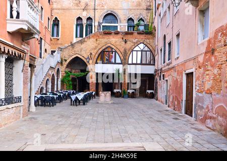 Venezia, Veneto, Italia. Vecchio cortile con un piccolo caffè all'aperto. Piccolo cortile vuoto, vecchie case in mattoni a Venezia, Italia. Foto Stock