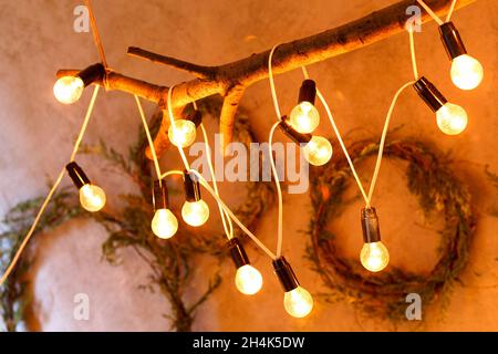 Lampadario a soffitto natalizio dal design originale, fatto di un ramo di albero secco e di una ghirlanda elettrica di lampade d'epoca Foto Stock