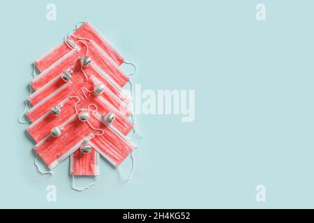 Albero di Natale alternativo fatto di maschere mediche e baubles vacanza argento su sfondo blu. Protezione contro i virus. Vista dall'alto. Banner.Crea Foto Stock