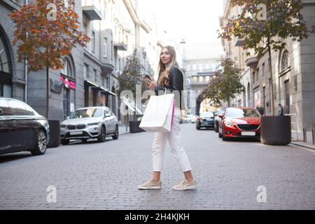 Donna che attraversa la strada nel centro della città, con le borse per lo shopping Foto Stock