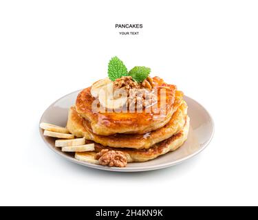 Le frittelle con banana, noci e menta vengono versate con succo d'acero in un piatto beige isolato su bianco. Vista laterale. Foto Stock