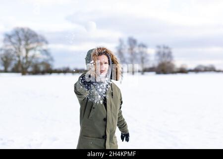 Un giovane uomo determinato che lancia una palla di neve verso la telecamera. Si trova in un paesaggio invernale coperto di neve Foto Stock