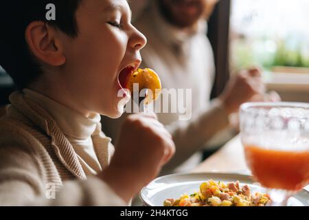 Primo piano del bambino di pasty ragazzo che mangia patate fritte seduto al tavolo del banchetto della cena durante le feste di famiglia. Foto Stock