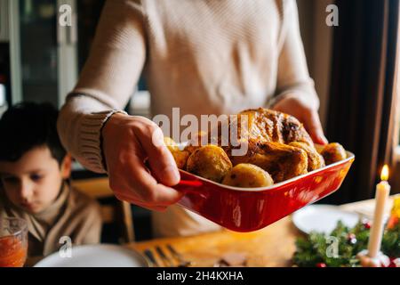 Vista laterale ravvicinata del putting dish del giovane uomo con tacchino caldo alla griglia sul tavolo della cena servito per feste di famiglia di Natale Foto Stock