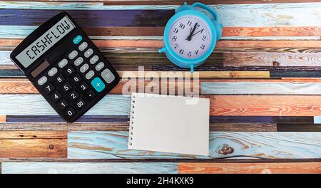 Calcolatrice con le parole flusso di cassa, accanto a loro si trova una sveglia, un blocco note per scrivere su un tavolo di legno Foto Stock
