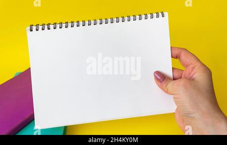 La mano della donna tiene un blocco note vuoto per la scrittura. I notepad colorati sono su sfondo giallo. Spazio di copia Foto Stock