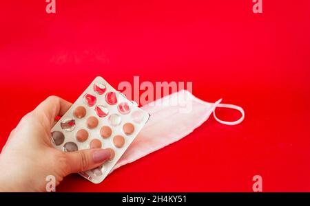 Pillole in mano di una donna su sfondo rosso, accanto a una maschera medica. Concetto di medicina. Foto Stock