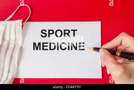 Il testo medico di medicina dello sport scrive su carta, accanto ad una maschera medica su sfondo rosso. Concetto di business per il trattamento e la prevenzione degli spor Foto Stock