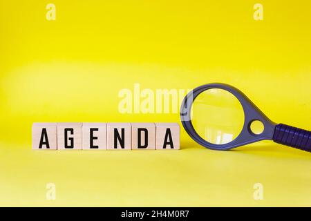 Agenda - parole fatte da blocchi di legno con lettere, elenco di argomenti del programma concetto, su sfondo giallo lente di ingrandimento Foto Stock