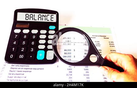 Calcolatore con la parola BALANCE sul display . Mano che tiene una lente d'ingrandimento sopra i rapporti finanziari Foto Stock