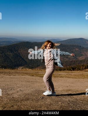 Una giovane donna in un vestito caldo e una giacca in denim gioisce in montagna. Autunno in montagna. Ragazza felice. Natura e viaggi. Foto verticale. Foto Stock