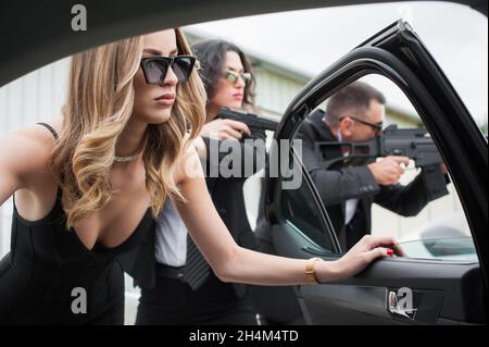 Il team armato professionale di guardie del corpo femminili e maschili protegge la persona della celebrità in limousine auto. Bodyguard e protezione personale VIP. Professate Foto Stock
