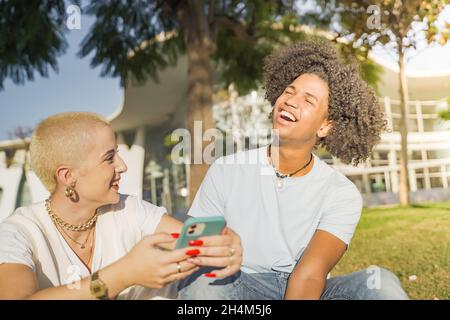 La coppia Afroamericana e caucasica ridendo, guardando il telefono e ascoltando la musica in città. Foto Stock