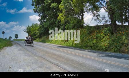 Ronks, Pennsylvania, 2021 giugno - Amish Open Horse and Buggy si avvicina con una coppia e una figlia in esso in una giornata di sole Foto Stock